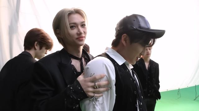 Felix is squeezing Changbin's shoulders. He is still smiling but not as brightly as before, and there might be a touch of worry.