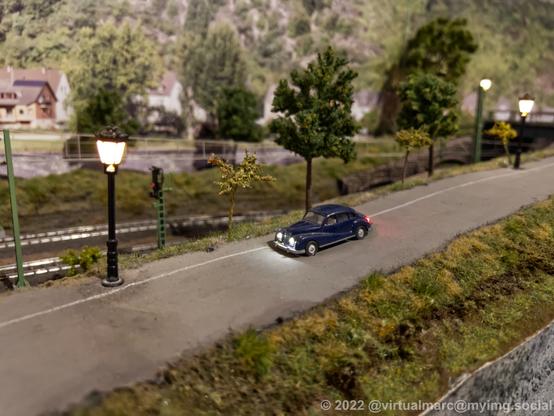 A photo of a model railway with an old car on a road.