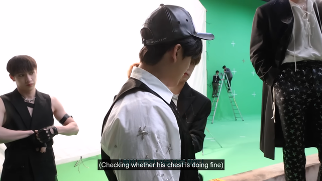 Side view of Changbin, with Seungmin touching his chest. Bang Chan stands behind them, adjusting his gloves, looking at Seungmin with his head tilted a little to the side. Chan's expression might be a little sour?? Caption: (Checking whether his chest is doing fine)