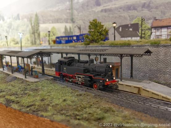 A photo of a steam locomotive with no wagons standing on a small model railway train station.