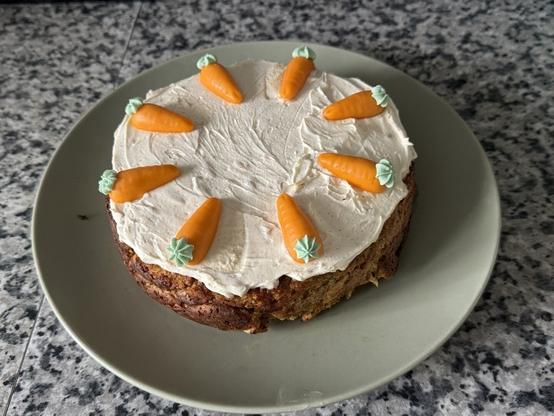 A carrot cake is topped with frosting and decorated with small icing carrots.