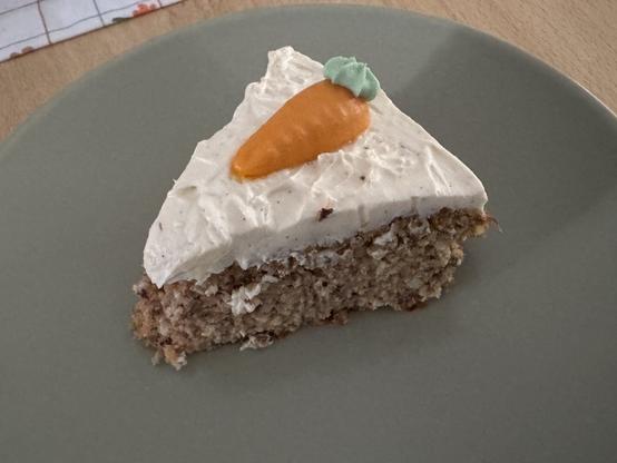 A slice of carrot cake topped with cream and a small carrot decoration sits on a green plate.