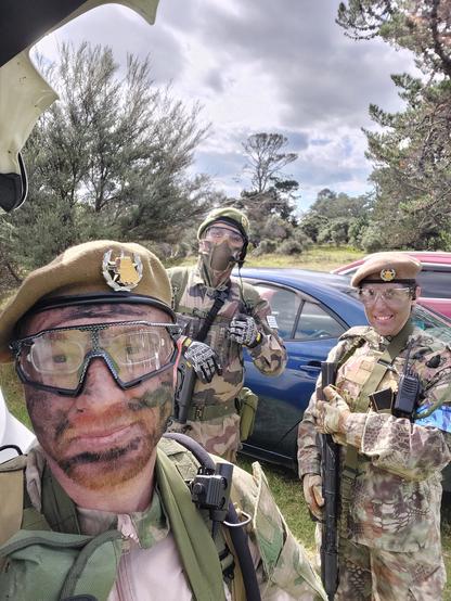 Selfie de tres personas uniformadas, con boinas color khaki y el emblema de un capibara empuñando una pistola. Los chicos se ven sonriendo y levantan los pulgares.