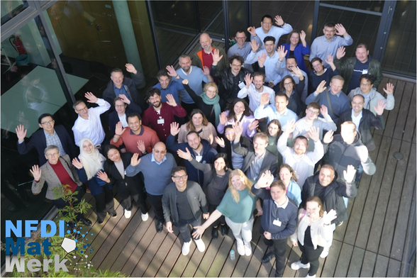 Participants of the NFDI-MatWerk All hands on Deck Meeting in Siegburg. The picture was taken from a balcony and the c. 40 participants are looking up to the photographer, waving their hands smiling.