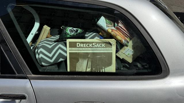 Zugemülltes Auto, darin Zeitung mit Titel: „Drecksack“