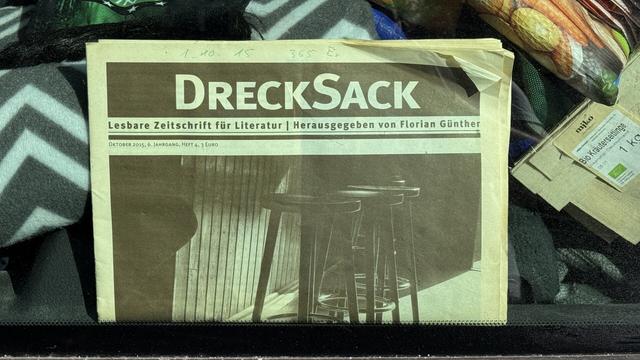 Zugemülltes Auto, darin Zeitung mit Titel: „Drecksack“ Näher dran