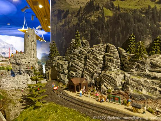 A photo of a castle ruin behind a small train station of a model railway.