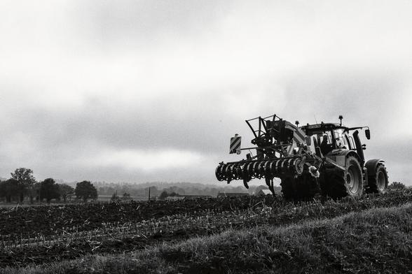 A tractor ploughs its furrow in a field. The photo was taken from a low angle on a cloudy day.