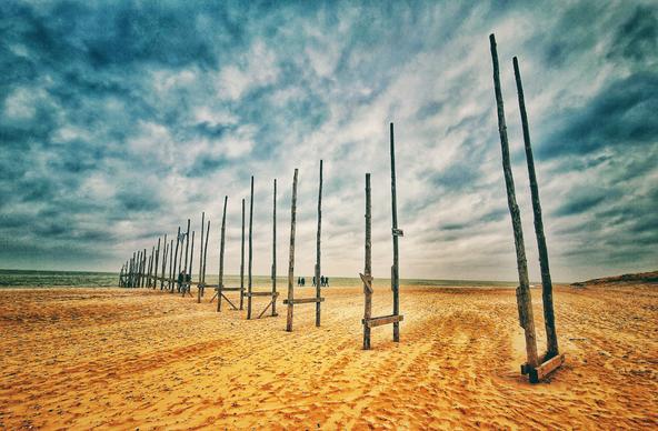 Farbiges Bild mit Blick über den Strand bei Texel in den Niederlanden im Bild verläuft eine Reihe doppelte Holzpfähle bis ins Meer.

Colored picture with view over the beach near Texel in the Netherlands in the picture a row of double wooden piles runs into the sea