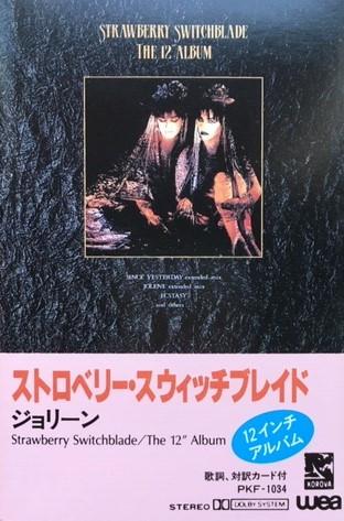 The cover of Straberry Switchblade's The 12 Inch Album on cassette. A candlelit photo of Rose and Jill is on a slate textured background, with Japanese writing below