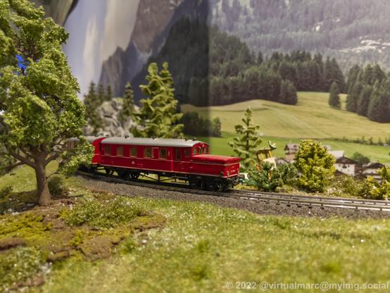 A photo of a red passenger train on a model railway in a rural area.
