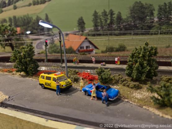 A photo of a model railway with a cabriot car getting repared and an ADAC car standing next to it.