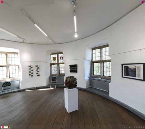 a room in a medevial building. The floor ist made of oak and there's threee windows with stone frames in the thick walls. The walls and roof are white. there's some pictures hanging on the walls and a sculpture in the cnetre of the picture