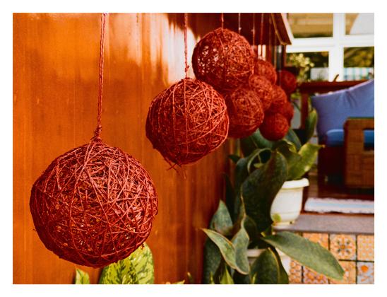 Hanging red yarn balls with some flowering plants in the background.