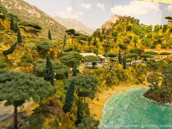 A photo of a coastal area with sand, hills and some buildings, probably a holiday resort, near water on a model railway.