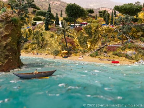 A photo of a beach on a model railway with hills and a rowing boat.