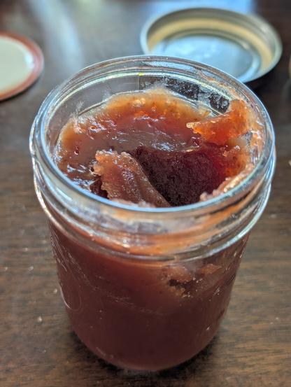 A jar of plum jam on a wooden table.