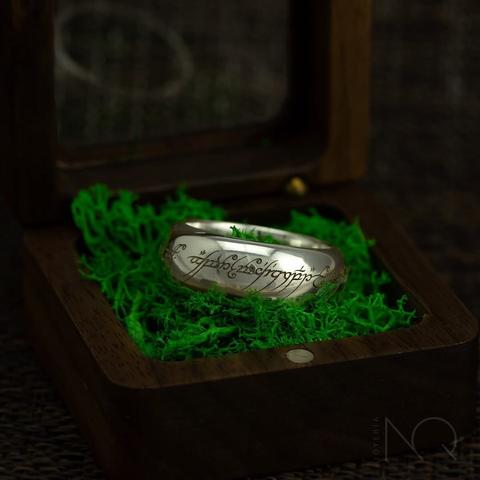 foto de mi versión del anillo único de el señor de los anillos en un a caja de madera  sobre liquen, con la inscripción élfica y en color plateado