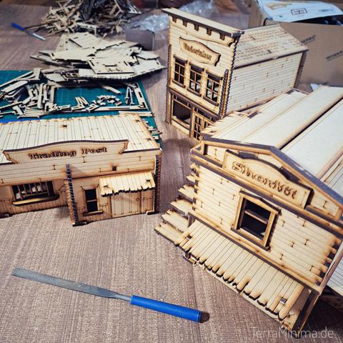3 fertig zusammengebaute Western Häuser in Miniaturformat. Alle aus gelasertem Holz.
Im Hintergrund ein Berg Einzelteile.