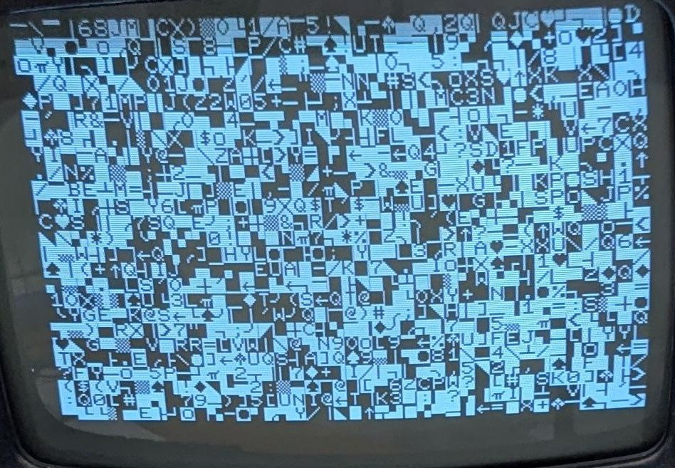 A closeup of the screen, showing random characters. Not just letter and numbers, but strange symbols such as card suits, gray rectangles, circles, and lines. Half the characters are black on white and half are white on black. (Actually more bluish than pure white.)