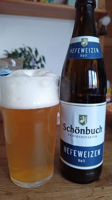 Auf einem Holztisch steht eine kleine Flasche Bier und ein gefülltes Glas mit hellgelben Bier