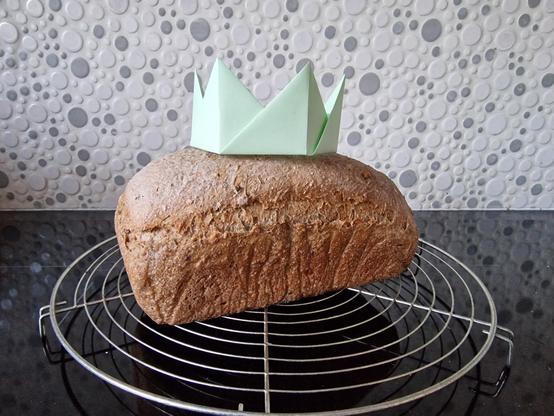 Loaf of bread cooling on a rack, with a light green origami crown on top of it.