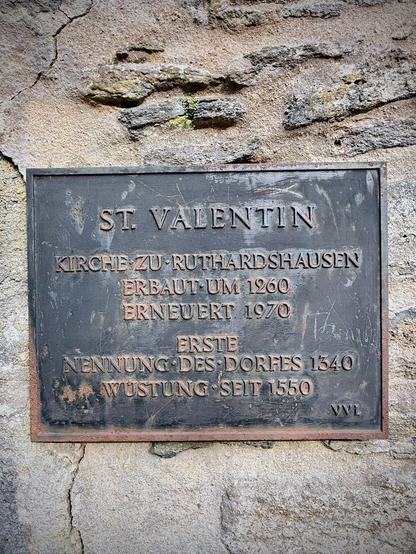 Nahaufnahme der Gedenktafel an der Innenwand der Kirchenruine St. Valentin. Die Inschrift nennt die Bauzeit um 1260, eine Erneuerung 1970 sowie die erste Nennung des Dorfes Ruthardshausen im Jahr 1340. Das Dorf wurde um 1550 zur Wüstung.