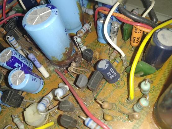 Close up of light blue capicitors with brown goo and rust like stuff were they are placed on the pcb