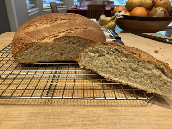 A loaf of bread about 3” tall and 8 wide. Golden crust. Sitting on a wire rack on a wooden cutting board.