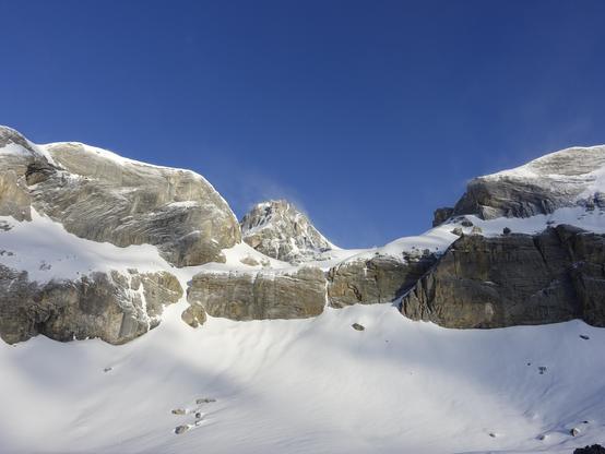 The wind gust over the rocky summits transports snow so it seems as it would have fresh snow. A dark blue sky.