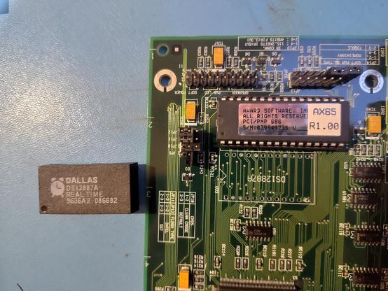 Close up picture of the corner of a Pentium Pro motherboard.
The battery-integrated RTC chip has been desoldered and lies next to the motherboard.