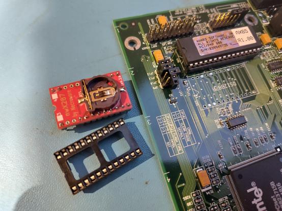 Close-up picture of a corner of a Pentium Pro motherboard.
The battery-integrated RTC chip has been removed. Next to the motherboard lie a 24 pin DIP socket, and a small red PCB with a battery holder.