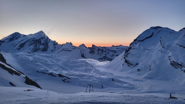 The sunrise in front of the hut draws an orange background behind the mountains. Clouds crawling over the Gemmi to fall down to Leukerbad.
