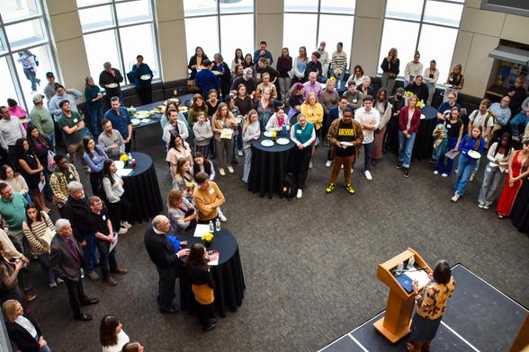 Overhead shot of some 60 people around a lectern listening to announcements.