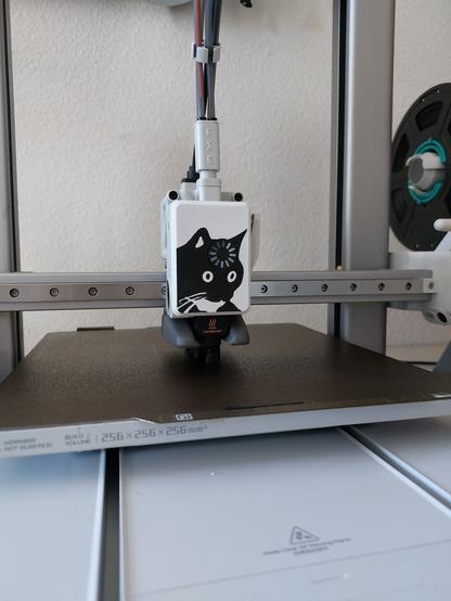 Extruder of a bamboo lab 3D printer. The front cover depicts the thinking cat meme, which is a black cat staring into the distance, outspaced, with a loading circle icon over its head. The icon is connected to the extruder motor shaft, which makes it turn as the printer prints, making it look like the cats thoughts are loading.