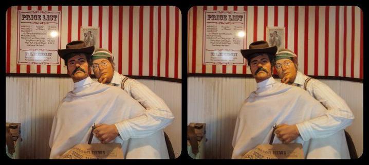 Barber at Enchanted Forest. Barber is pondering how to shave a mustachioed cowboy. Cowboy, in the barber chair, still has his hat on.