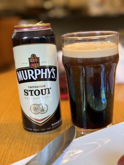 A pint can of Murphys stout, black with a tan field and a red and black shield. A pint glass full of dark beer is to the right
