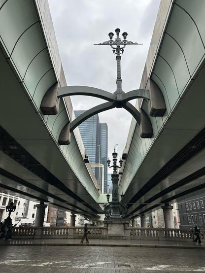 A lamp post suspended oddly over a bridge, mounted on an asymmetrical set of girders between two arms of an expressway
