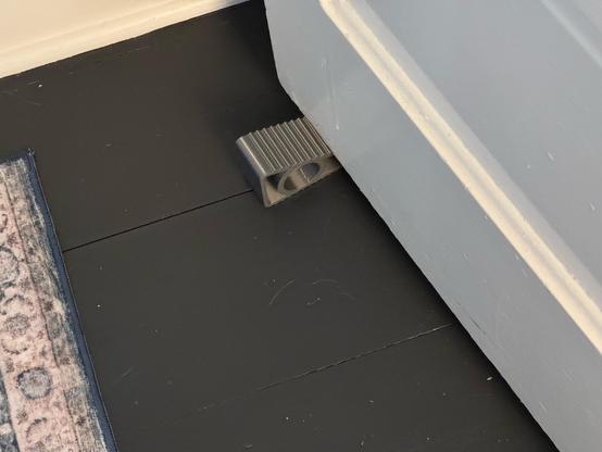 A dark gray wedge sitting on the floor, holding a door open.