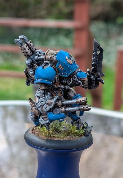 A painted mini of a steampunk robot from the game Warmachine, in blue, brass, and silver.