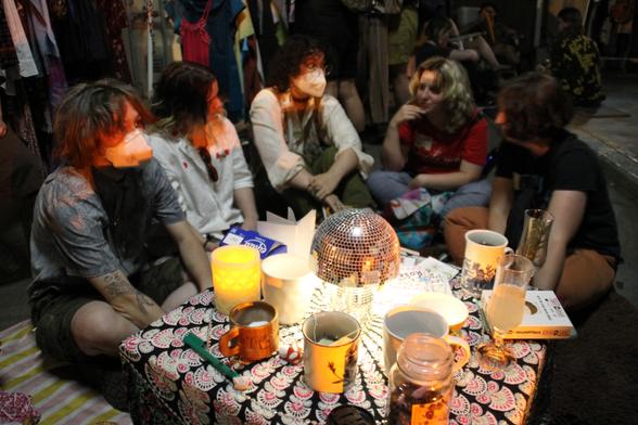 Young people sitting around a low table stacked with tea, focussing on a conversation that is playing out