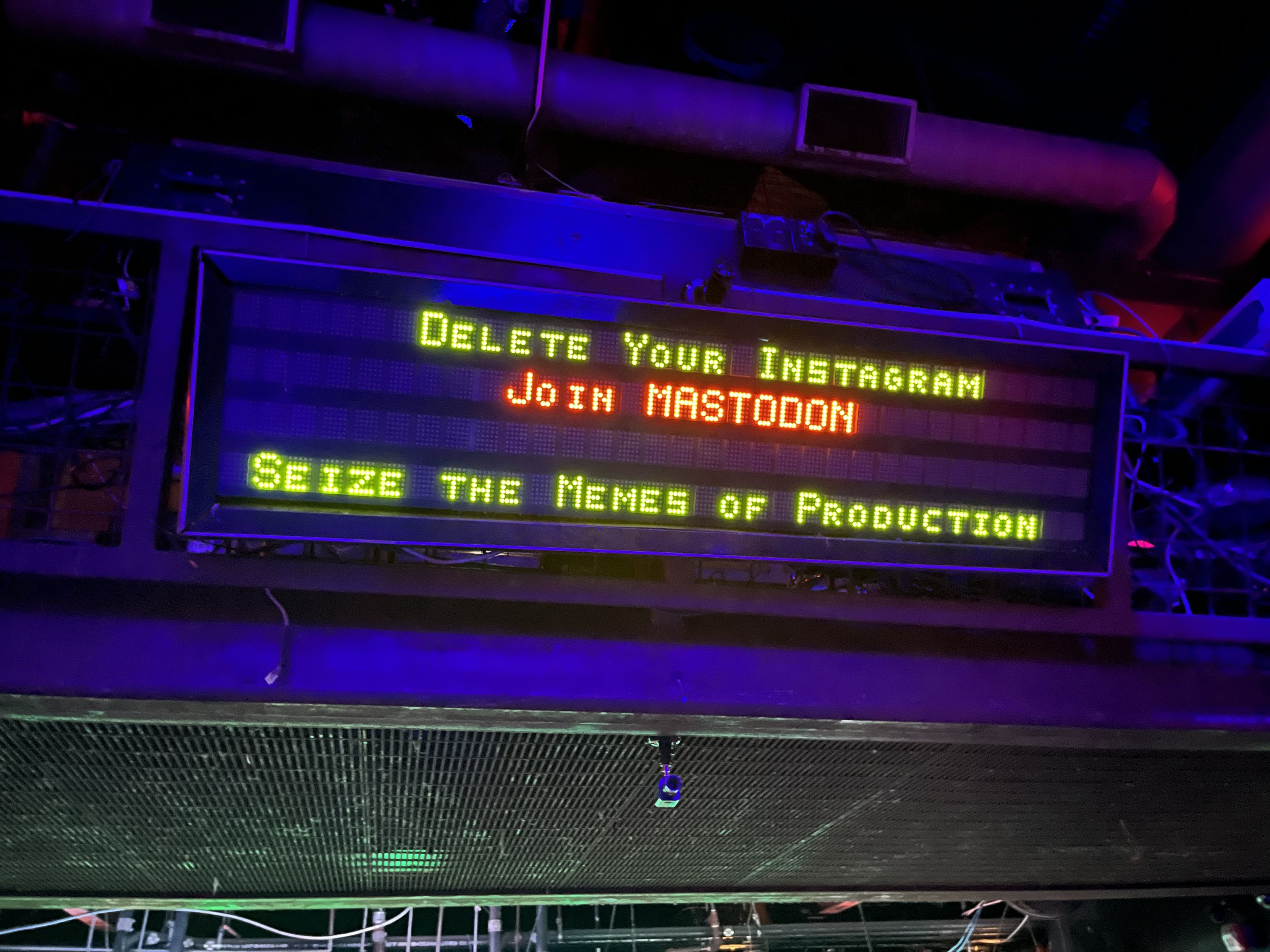 An illuminated LED sign with the text “Delete your Instagram” “Join Mastodon” and “Seize the memes of production”