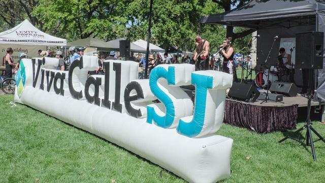 The main vivacalle San Jose sign. Its a inflatable white sign with the words in back letters and the SJ is in blue.
There is a stage and a local band in the background.