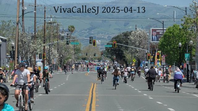 A busy 6lane street full of bikes as far as the eye can see. Green hills rise in the background.