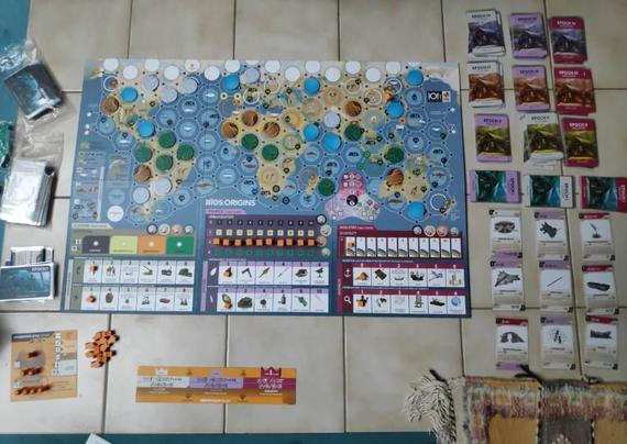 Plateau  de jeu de BIOS : Origines, début de partie. Une carte du monde avec de héros cercles pour les emplacements. Des tableaux d'avancement culturels, politiques et industriels. Des cartes pour les idées que l'humanité naissante va développer.