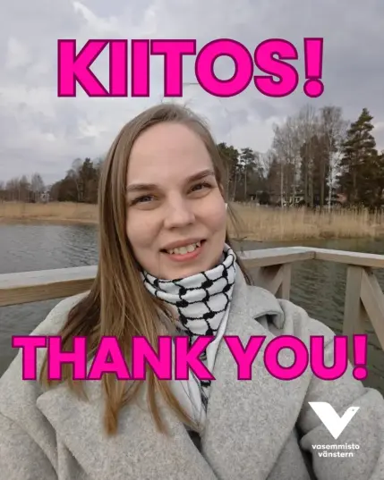Hynyilevä Elina merellä. Harmaa takki ja palestiinalaishuivi. Teksti "Kiitos Thank you" pinkillä. Vasemmistoliiton valkoinen logo.
