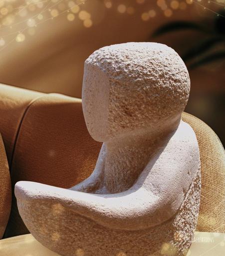 Une sculpture en pierre blanche représente une silhouette simplifiée, sans visage, les bras tendus.