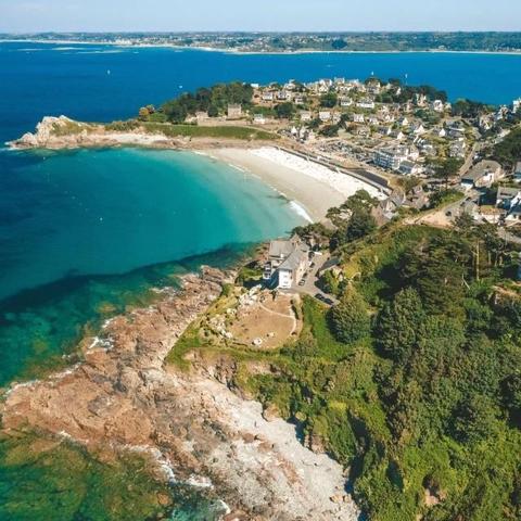 Aerial view of Trestignel Beach featuring a serene beach with turquoise waters, rocky cliffs, and a residential area with scattered houses surrounded by greenery. The hill is now fully urbanised compared with one century ago