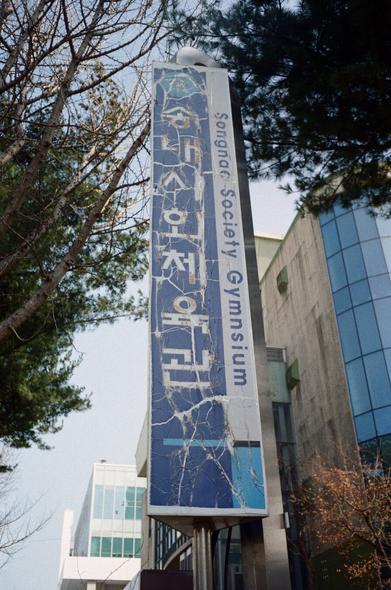 세로로 길쭉한 '송내사회체육관' 간판. 오래되어 글씨와 도장이 잔뜩 벗겨지고 금갔다.