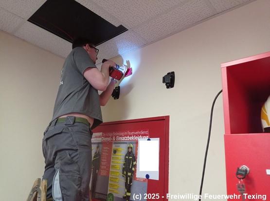 Eine Person auf einer Leiter befestigt an der Wand eine Haltevorrichtung für einen Computermonitor